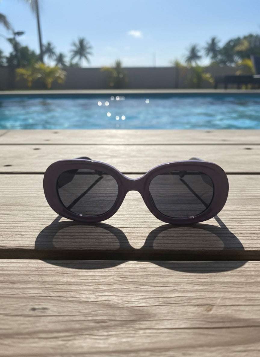 Lilac oval sunglasses with dark lenses placed beside a swimming pool under bright sunlight — Grape Crush Sunglasses by VA RA.