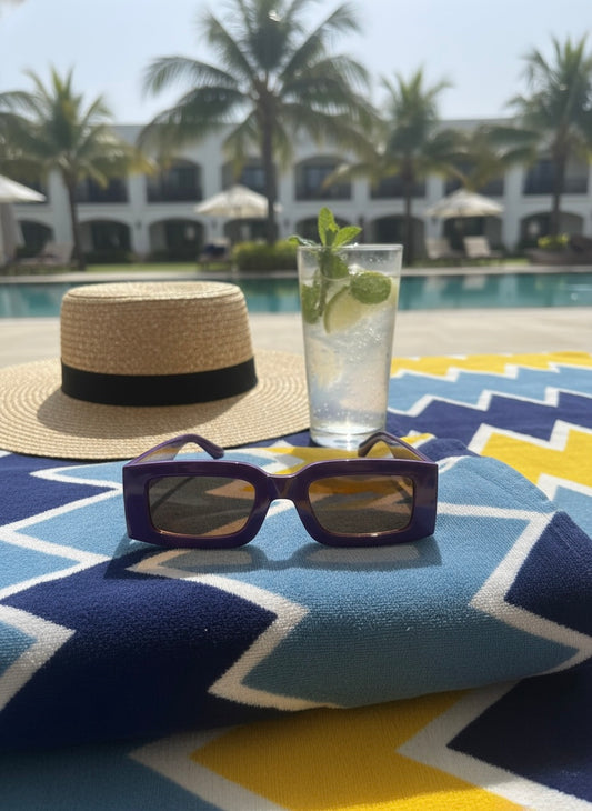 Purple rectangular sunglasses placed on a colourful beach towel beside a pool and mint cocktail — Blackberry Martini Sunglasses by VA RA.