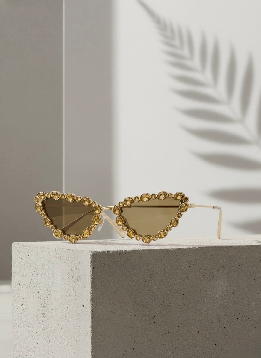 Gold crystal-rimmed cat-eye sunglasses on a concrete block with palm shadows — Golden Daiquiri Sunglasses by VA RA.