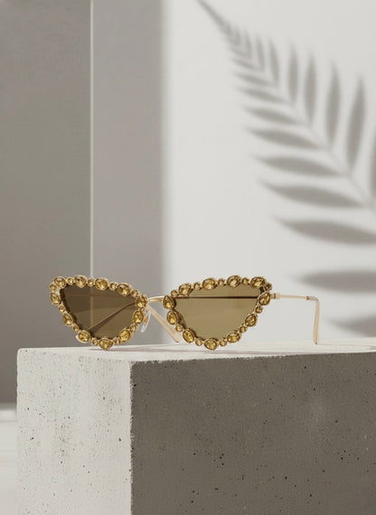 Gold crystal-rimmed cat-eye sunglasses on a concrete block with palm shadows — Golden Daiquiri Sunglasses by VA RA.