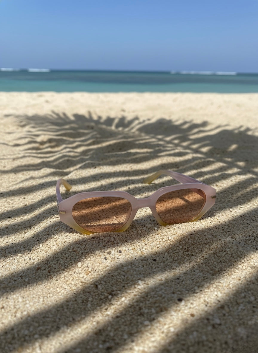 Pina Colada Sunglasses placed beside a coconut drink on a white beach with turquoise water — resort eyewear by VA RA.