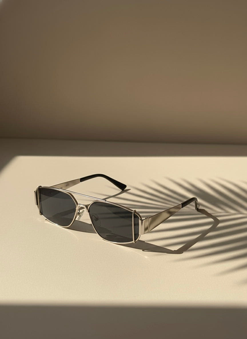 Silver metal sunglasses with smoky black lenses resting on a sunlit surface with palm shadows — Silver Highball Sunglasses by VA RA.