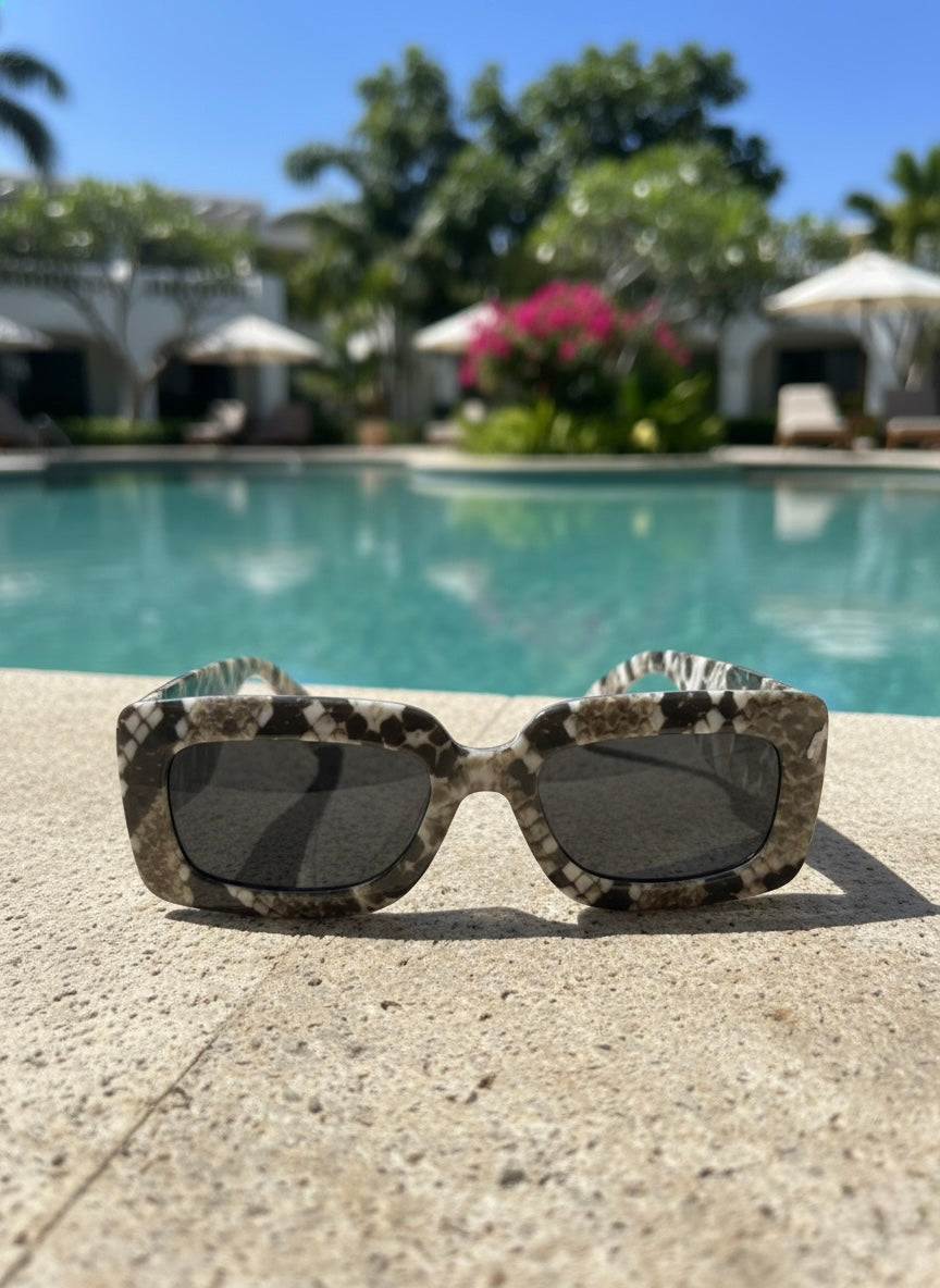 Snakeskin sunglasses with smoky lenses placed beside a turquoise pool under bright sun — VA RA Black Mojito Sunglasses.