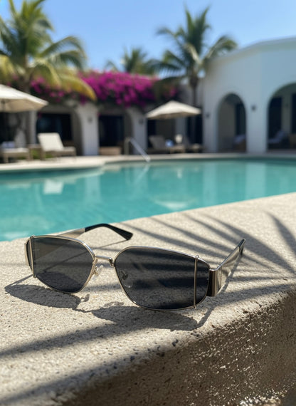 Metallic silver sunglasses placed beside a turquoise resort pool under bright sunlight — VA RA Silver Highball Sunglasses.